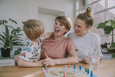 Fröhliche Mütter schauen zu, während ihr Sohn zu Hause ein Brettspiel spielt - MFF06661