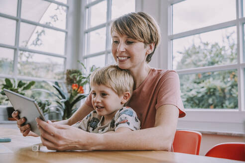 Mutter benutzt digitales Tablet mit ihrem Sohn, während sie zu Hause sitzt - MFF06663