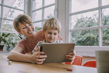 Mutter hält digitales Tablet mit Sohn, während sie zu Hause sitzt - MFF06664