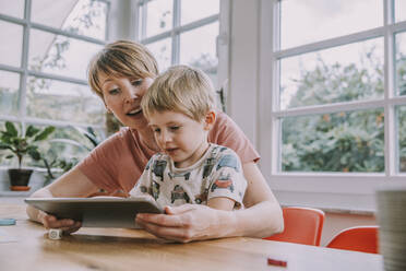 Mutter und Sohn benutzen ein digitales Tablet, während sie zu Hause sitzen - MFF06665