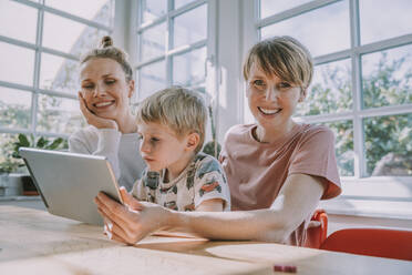 Happy mothers using digital tablet with son while sitting at home - MFF06666