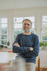 Smiling mature man with arms crossed standing at home - MFF06687