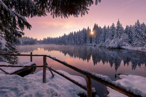 Scenic Winterlandschaft der ruhigen See mit hölzernen Pier mit Schnee und Nadelwald bedeckt reflektiert im Wasser in Sonnenuntergang Zeit, lizenzfreies Stockfoto