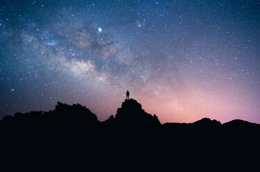 Silhouette eines Mannes von Wanderern, der auf einem dunklen Felsen vor einem sternenklaren Nachthimmel in langer Belichtung auf Teneriffa steht - ADSF17118