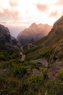 Malerischer Blick auf eine serpentinenförmige Asphaltstraße durch felsige, mit Grünpflanzen bewachsene Berge am Morgen auf Teneriffa - ADSF17136