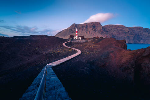 Windungspfad zum Leuchtfeuer auf einem Hügel nahe dem Meer vor dem Hintergrund der Berge am Morgen auf Teneriffa - ADSF17140