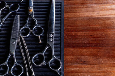 From above of vintage kit of various hair cut scissors and clamp arranged on black board on shabby wooden table - ADSF17150