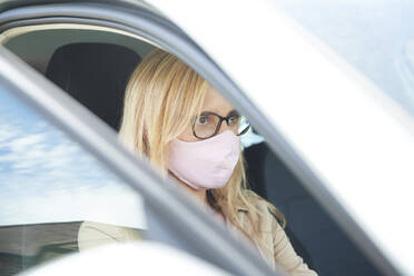 Mature woman wearing protective face mask sitting in car - PMF01441