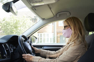 Ältere Frau mit Gesichtsschutzmaske beim Autofahren - PMF01442