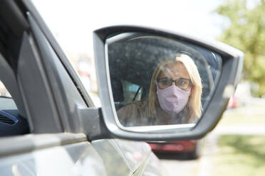 Reflection of woman wearing protective face mask sitting in car - PMF01444