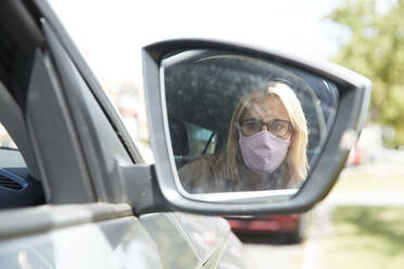 Spiegelung einer Frau mit Gesichtsschutzmaske, die im Auto sitzt - PMF01444