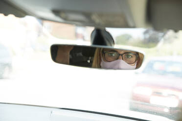 Spiegelung einer reifen Frau mit Gesichtsschutzmaske, die im Auto sitzt - PMF01445