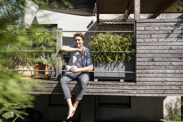 Man with coffee cup sitting in balcony on sunny day - UUF21853