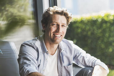 Mid adult man smiling while sitting in house - UUF21870