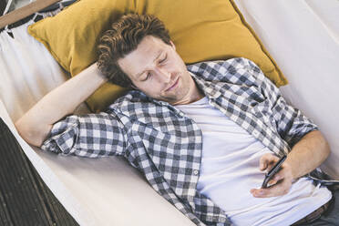 Man text messaging on smart phone while lying on back at home - UUF21881