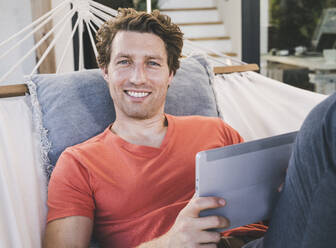 Mittlerer erwachsener Mann liegt in der Hängematte und benutzt zu Hause ein digitales Tablet - UUF21886