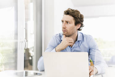 Mid adult man using laptop looking away while sitting in office - UUF21889