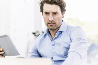 Man concentrating while using digital tablet sitting in office - UUF21899