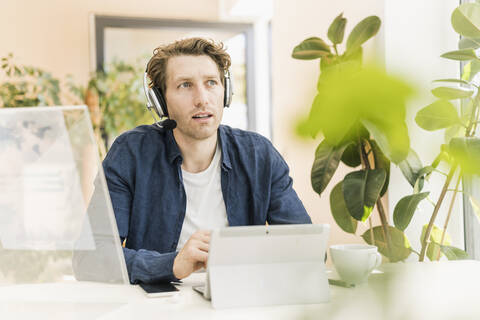 Mid adult man wearing headphone looking away while sitting at home stock photo