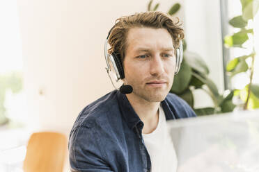 Mid adult man listening music through headphone sitting at home - UUF21911
