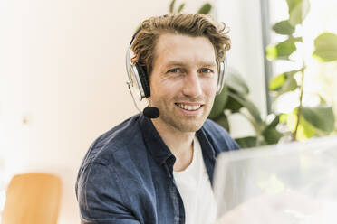 Smiling mid adult man wearing headphone sitting at home - UUF21912