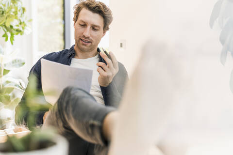 Mid adult man writing on paper while sitting at home stock photo