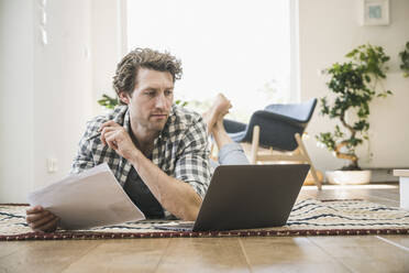 Mittelgroßer erwachsener Mann liegt auf der Vorderseite und benutzt einen Laptop zu Hause - UUF21934