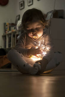 Cute baby girl holding christmas light while sitting at home - SKF01596