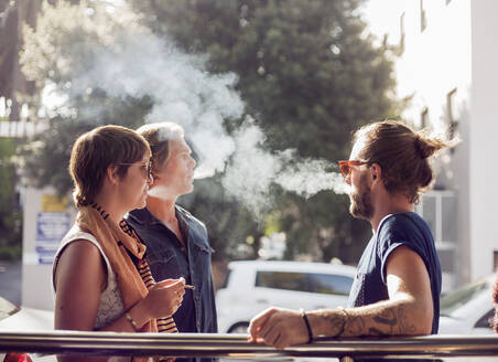 Freunde beim Rauchen im Freien an einem sonnigen Tag - AJOF00383