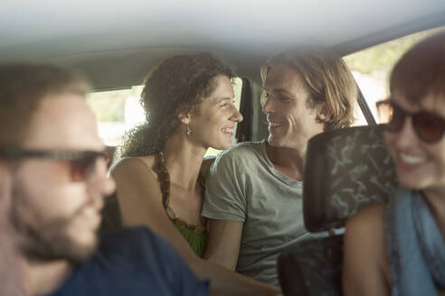 Lächelndes Paar mit Freunden im Auto sitzend während einer Autoreise - AJOF00402