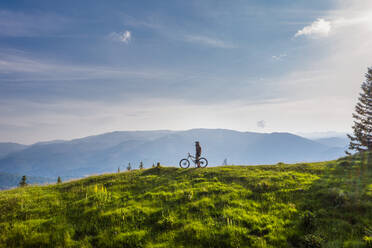 Mountain biker on his bike on a green hill on a sunny day - CAVF89781