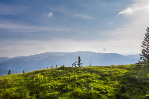 Mountainbiker auf dem Fahrrad auf einem grünen Hügel an einem sonnigen Tag - CAVF89781