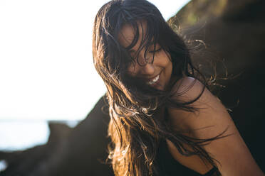 Young Latina Woman laughing by the ocean at golden hour in summertime - CAVF89786