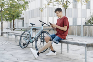 Man with disability using smartphone near bicycle - CAVF89797