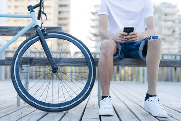 Behinderter Fahrradfahrer surft mit seinem Smartphone in der Stadt - CAVF89800