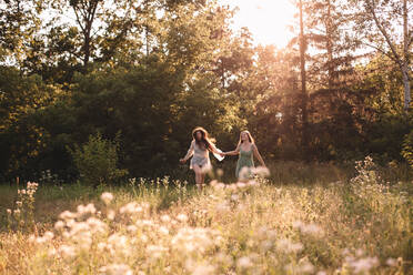 Happy lesbian couple holding hands while running in forest in summer - CAVF89833