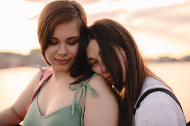 Portrait of happy lesbian couple standing on bridge at sunset - CAVF89844