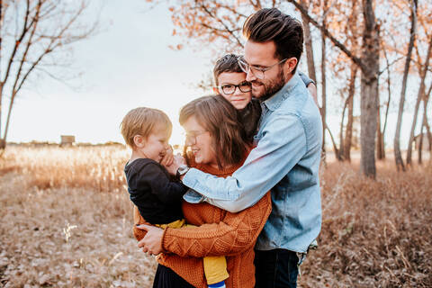 Fashionable young family hugging in a field on a cool autumn evening stock photo