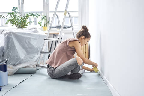 Young woman applying adhesive tape on wall while sitting at home stock photo