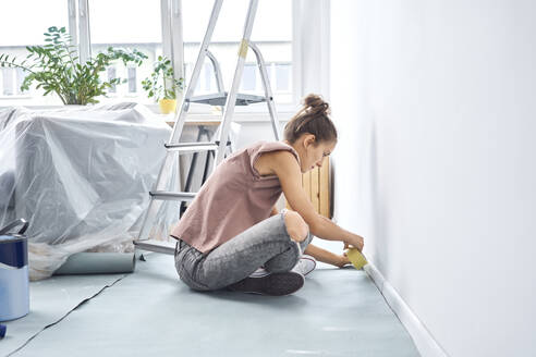 Junge Frau klebt Klebeband an die Wand, während sie zu Hause sitzt - BSZF01720