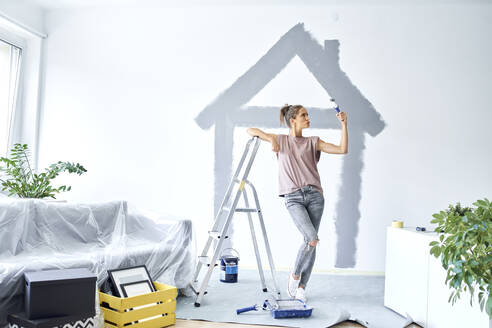 Young woman with paint roller doing pout while leaning on ladder at home - BSZF01728