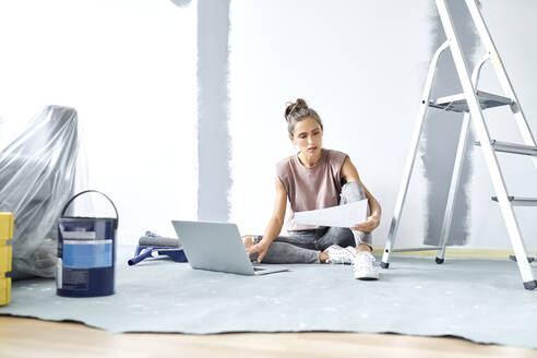 Young woman holding paper while working on laptop at home - BSZF01733