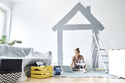 Smiling woman working on laptop while sitting against wall at home - BSZF01734