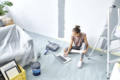 Woman with paper working on laptop while sitting at home - BSZF01735