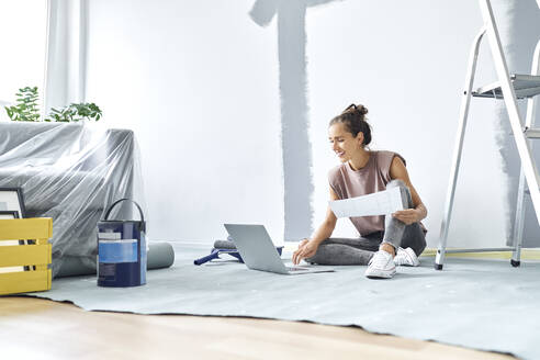 Smiling woman sitting on floor while working on laptop at home - BSZF01736