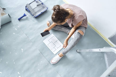 Smiling woman looking at paper while using mobile phone at home - BSZF01738