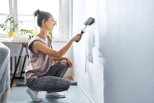 Woman smiling while painting wall at home - BSZF01748