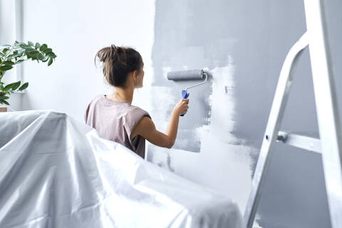 Young woman using paint roller while painting wall at home stock photo