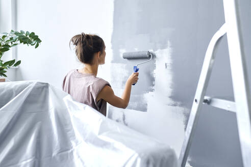 Young woman using paint roller while painting wall at home - BSZF01749