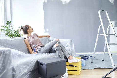 Woman with paint roller looking at wall while sitting on sofa at home stock photo